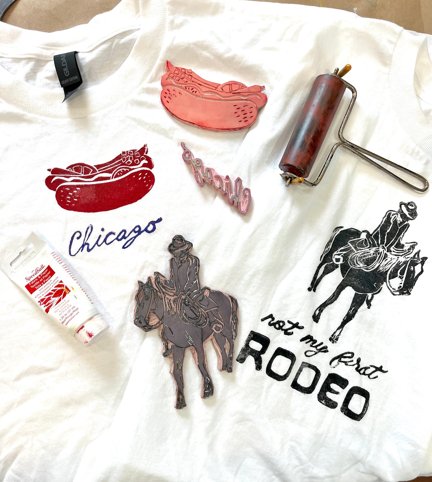 White t-shirt with printed designs including a hot dog, 'Chicago', a cowboy on a horse, and 'not my first RODEO'.