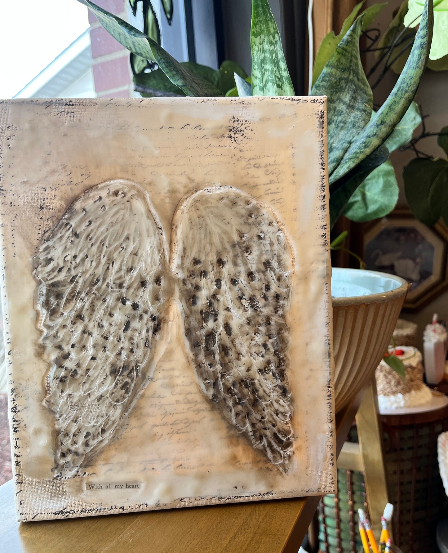 Mixed media angel wings on canvas next to a plant on a wood surface
