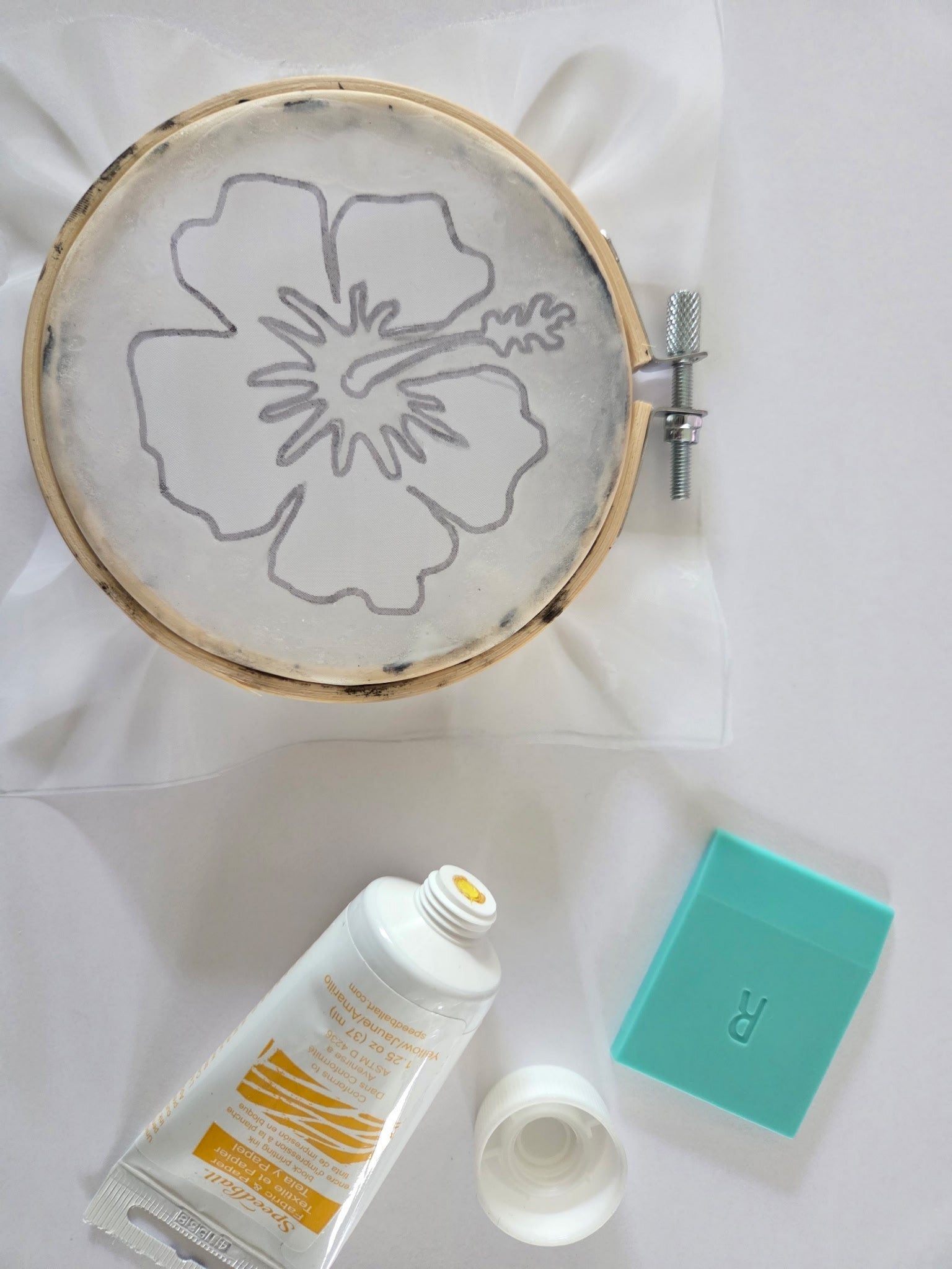 Embroidery hoop with floral design on a white surface next to a bottle of lotion and a turquoise box.